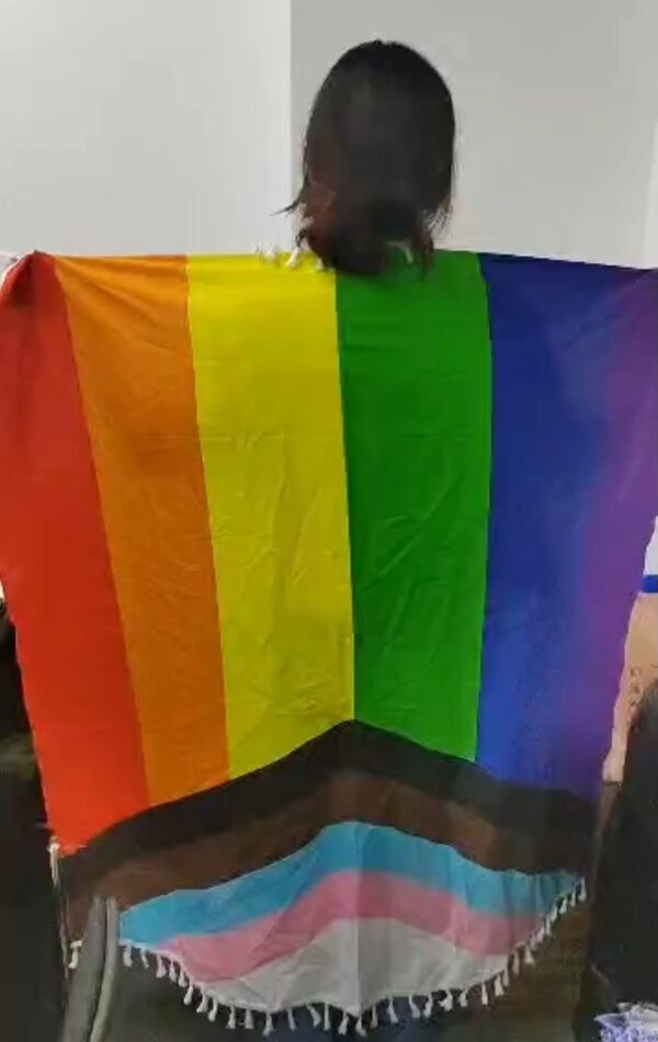 A woman holding the LBTQ+ Keffiyeh spread behind her back.